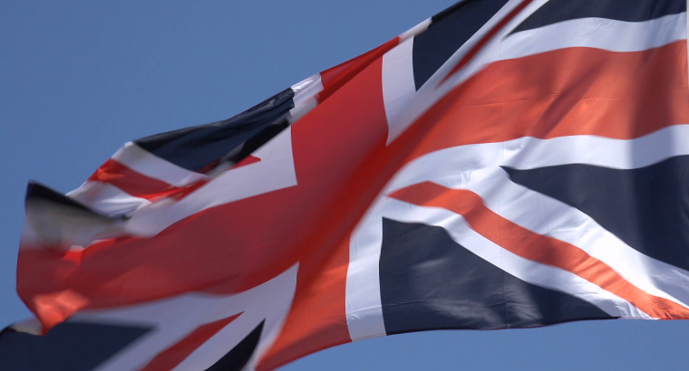 zoom-in-british-flag-blowing-in-wind-with-blue-sky-background-britain_4yzqufnng__F0006